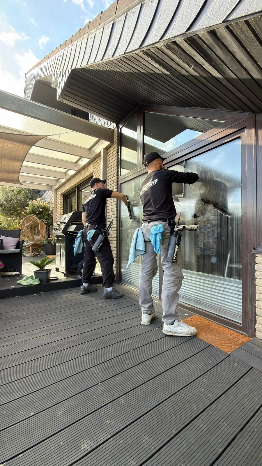 Zwei Mitarbeiter waschen große Fensterflächen an einer Terrasse ein